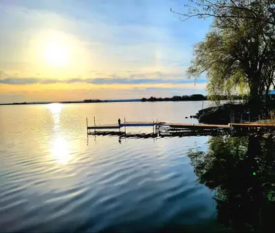 a dock on a lake with the sun setting at Waterfront Comfy Guesthouse, PEC in Carrying Place
