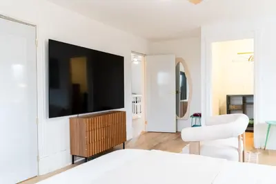 a white bedroom with a flat screen tv on a wall at County Cove - Newly Renovated Century Home in Carrying Place
