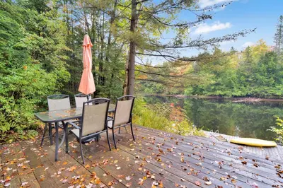 a table with chairs and an umbrella next to a river at Muskoka Waterfront Cottage with Canoes and Fire Pit in Huntsville