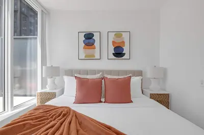 a white bedroom with a bed with orange pillows at Prime 2BR Condo with Massive Patio & Parking in Toronto