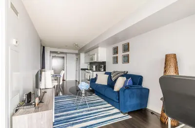 a living room with a blue couch and a kitchen at Spacious 1 Bedroom plus Den Condo Iceboat Terrace Downtown Toronto in Toronto