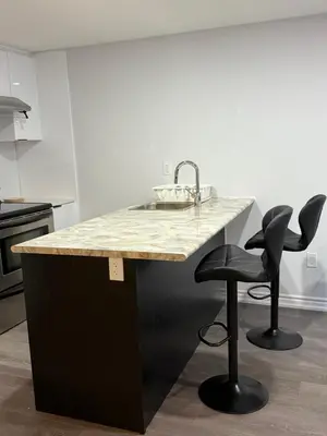 a kitchen with a sink and two bar stools at Comfy Basement Suite in Quiet Neighbourhood in Whitby