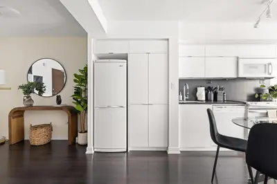 a white kitchen with a table and a refrigerator at Stylish 1BR Condo with Patio Steps from Waterfront in Toronto