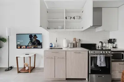 a kitchen with white cabinets and a tv on the wall at Modern Studio-Style Condo in Downtown Toronto in Toronto