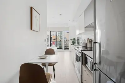 a white kitchen with a table and a refrigerator at Modern Studio-Style Condo in Downtown Toronto in Toronto