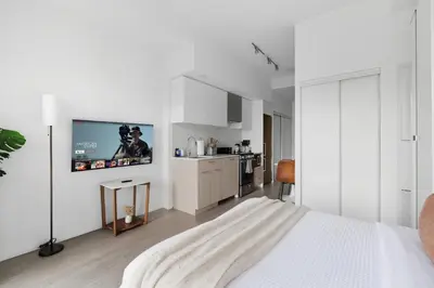 a white bedroom with a bed and a tv on the wall at Modern Studio-Style Condo in Downtown Toronto in Toronto
