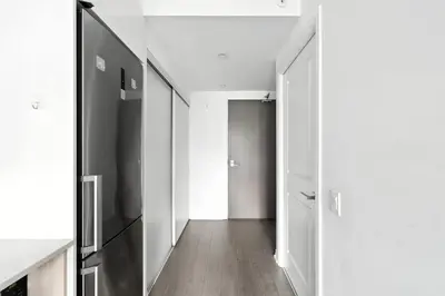 a hallway with white walls and a black refrigerator at Luxe Downtown Studio Near Eaton Centre & Transit in Toronto