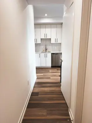 a hallway of a kitchen with white cabinets and wood floors at LuxCondo in the Downtown Kitchener Uptown Waterloo in Kitchener