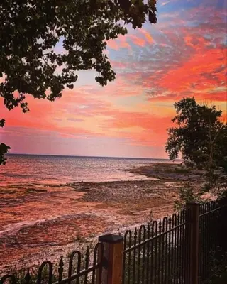 a sunset over a beach with a fence and the ocean at Crystal Beach Executive Waterfront Lakehouse in Fort Erie