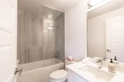 a white bathroom with a tub and a toilet and a sink at Modern 2BR Getaway with Balcony, BBQ and Parking in Innisfil