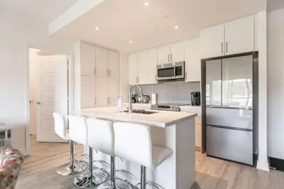 a kitchen with white cabinets and a island with bar stools at Modern 2BR Getaway with Balcony, BBQ and Parking in Innisfil
