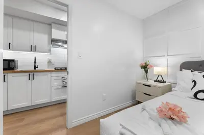 a white bedroom with a bed and a kitchen at High Park Grove Modern 1B1B, Kitchen, Laundry in Toronto
