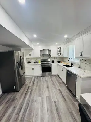 a large kitchen with white cabinets and wooden floors at Hearth & Home Spacious Suite in Pickering
