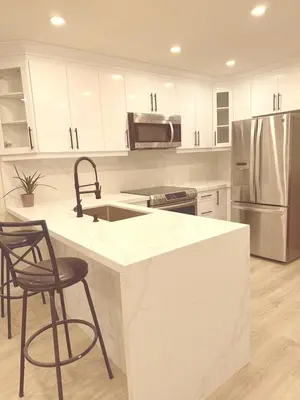 a kitchen with white cabinets and a counter with stools at Modern 1-BR Suite EV Charger, Backyard BBQ & Near Square One in Mississauga