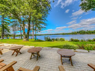 a patio with picnic tables and benches next to a lake at Private Lakefront Cottage Living on Muldrew Lake in Gravenhurst