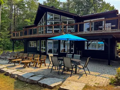 a house with tables and chairs and an umbrella at Private Lakefront Cottage Living on Muldrew Lake in Gravenhurst