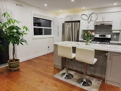 a kitchen with white cabinets and a kitchen island with chairs at Quiet Queen Bedroom near Finch Birchmunt in Toronto