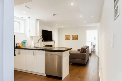 a kitchen with white cabinets and a living room at Bright 2 Bed Basement Near Square One Mall Family Friendly Stay in Mississauga