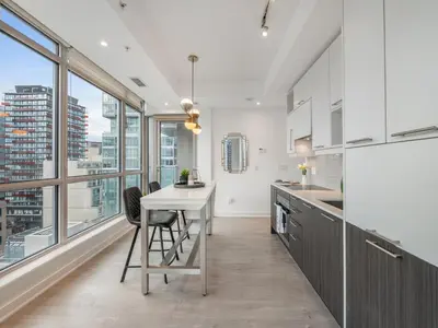 a kitchen with white cabinets and a table with a stool at VOGUE Suites Toronto Downtown - Entertainment District in Toronto