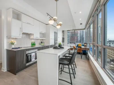 a kitchen with white cabinets and a bar with chairs at VOGUE Suites Toronto Downtown - Entertainment District in Toronto