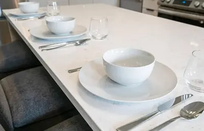 a table with white bowls and plates and silverware at 2 Brdm Modern Brand New Niagara Apt up to 6 ppl in Niagara on the Lake