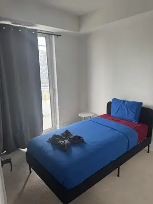 a bedroom with a bed with a blue blanket and a window at Lush 3 Bedroom Condo by CN Tower - Free Parking in Toronto