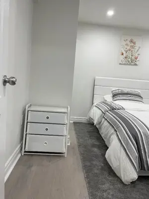 a white bedroom with a bed and a night stand at Rayann Hospitality in Toronto