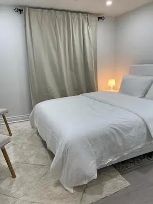 a bedroom with a large white bed and a chair at Hanan Hospitality in Toronto