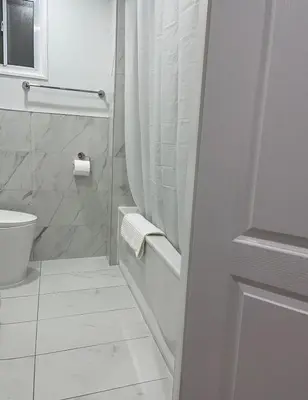 a white bathroom with a shower and a toilet at Hanan Hospitality in Toronto