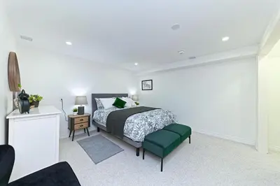 a white bedroom with a bed and a green ottoman at SPACIOUS & FULLY PVT-2BR UNIT ON GROUND LEVEl in Burlington