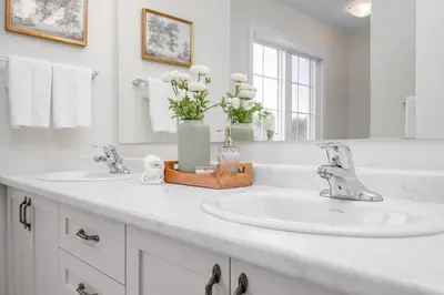 a white bathroom with two sinks and a vase of flowers at Stylish and Cozy Muskoka Vacation Home in Gravenhurst