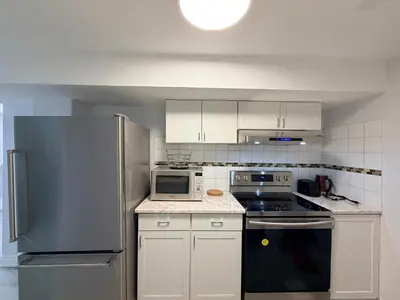 a kitchen with white cabinets and a stainless steel refrigerator at Modern Cozy Basement Suite Free Parking in Brampton
