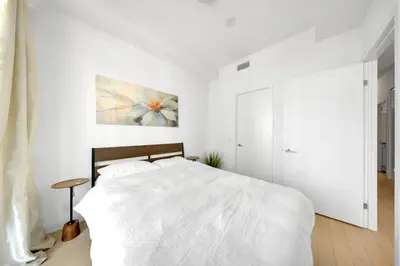 a white bedroom with a bed and a painting on the wall at Tranquil Lakeside Suite Toronto in Toronto
