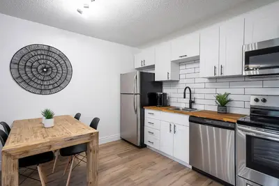 a kitchen with white cabinets and a wooden table at The Fox Den - Modern Condo Collingwood - Sleeps 5 in Collingwood