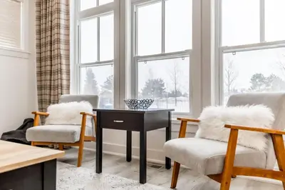 a living room with two chairs and a table and windows at Rivergrass Oasis Across from Blue Mtn Hot Tub in Blue Mountains