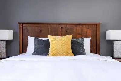 a white bed with a wooden headboard and two lamps at Three Suns Across Blue Mtn Hot Tub & Shuttle in Blue Mountains