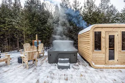 a hot tub next to a wooden house with snow at The Hideaway - Tiny House in Flesherton