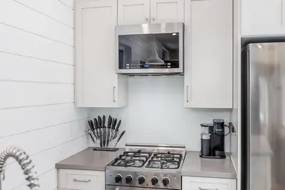 a kitchen with white cabinets and a stove top oven at The Hideaway - Tiny House in Flesherton
