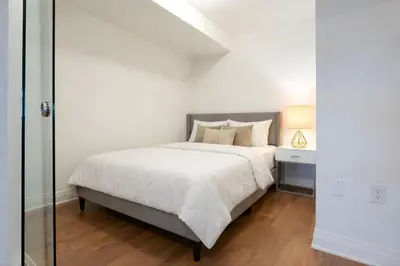 a white bedroom with a bed and a glass door at RivetStays - The Westmounts in Toronto