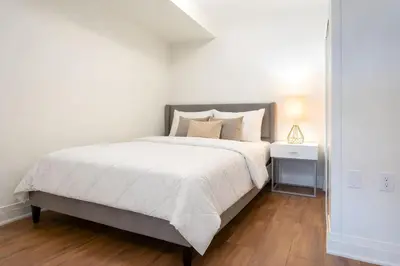 a white bedroom with a large bed and a night stand at RivetStays - The Westmounts in Toronto