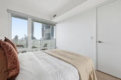 a white bedroom with a bed and a large window at Cozy 1BR Suite Steps to Subway City Views in Toronto