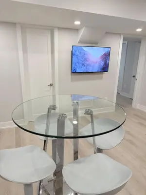 a glass table with two white chairs and a tv on a wall at Modern and Cozy Basement Suite,2 Bedrooms with Kitchen ,Parking and Separate Entrance in Milton