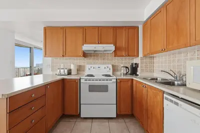 a kitchen with wooden cabinets and a white stove top oven at Elegant 2BR Sky Condo for 9 - Terrace - Lake Views in Mississauga