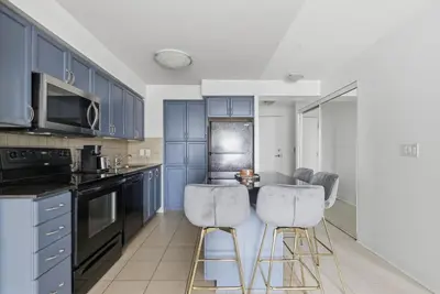 a kitchen with blue cabinets and bar stools at Designer 2BR - King Suite - Rare 2 Parking - YYZ in Mississauga