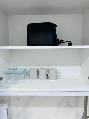 a white shelf with mugs and glasses on it at Studio Basement Suite with Sofa Bed and kitchen, Entrance from Garage -Sleeps 2 in Milton
