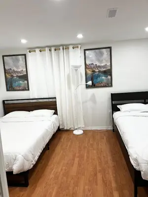 two beds in a room with white walls and wood floors at Stunning Partially Renovated Apartment in Toronto