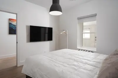 a white bedroom with a bed and a flat screen tv at Beam Loft in Beamsville