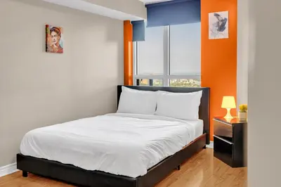 a bedroom with a bed with white sheets and an orange wall at 2 bedroom spacious apartment in Mississauga in Mississauga
