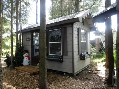 a small house with a porch in the woods at Cute Cozy Tiny House Surrounded by Trees for a Unique Couples Escape in Mt Forest, Ontario in Mount Forest