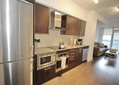 a kitchen with a stainless steel refrigerator and wooden cabinets at The Grand Avenue Suites - Downtown Toronto Entertainment District in Toronto
